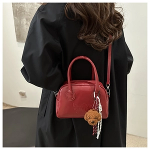 Detailed view of red leather crossbody bag with lucky embossed letters and poodle charm