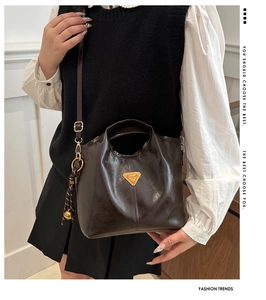 Close-up of brown glossy leather bucket bag with metallic logo and woven charm