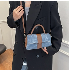 Detail of vintage blue denim handbag with brown leather trim held by a woman in a suit