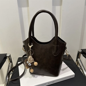 Borsa a secchiello vintage marrone scuro con ciondolo e tracolla su libro bianco