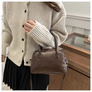 Brown vintage Boston bag with embossed lettering styled on a beige knit cardigan