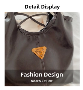 Detail shot of the dark brown leather texture and triangular brass brand nameplate