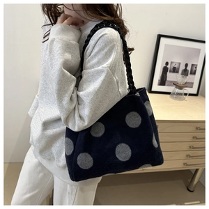 Detail of navy blue polka dot tote bag with thick black woven chain strap in home setting
