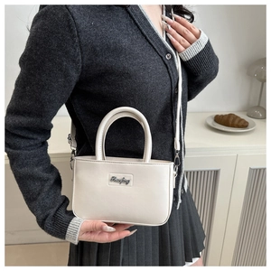 Detail of minimalist beige leather crossbody bag with metal logo and adjustable strap