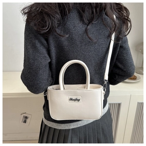 Detail of cream white mini crossbody bag featuring silver metal letter plate decoration