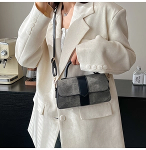 Close-up of grey suede crossbody bag with black leather strap on a cream blazer