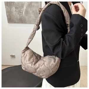 Detail of taupe quilted crossbody bag with floral pattern and knotted strap design