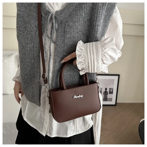 Detailed view of dark brown leather crossbody bucket bag with silver logo and top handles