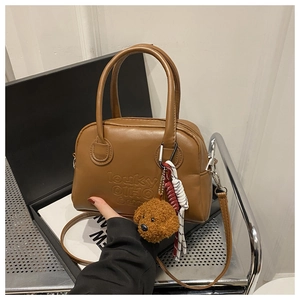 Detailed view of brown PU leather handbag featuring debossed letters and plush dog charm