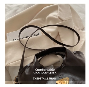 Close-up of dark brown tote bag with thin leather strap and brass metal brand plaque