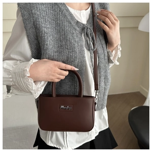 Detail of a dark brown faux leather handbag with silver logo plate and shoulder strap