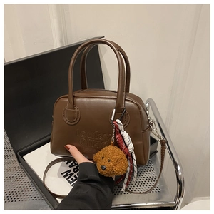 Detail of a brown leather handbag with embossed letters and a teddy bear charm
