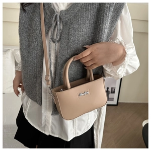 Close-up of beige minimalist crossbody bag with silver logo on white shirt model