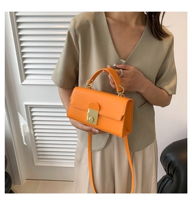 Detail of bright orange leather handbag with gold metal clasp and top handle