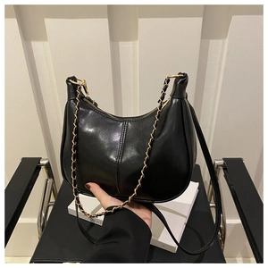 Detail of black semi-circle underarm bag with gold chain strap and polished leather finish