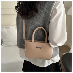 Detail of minimalist leather handbag featuring adjustable strap and metallic logo plate