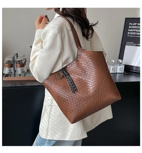 Detail of dark brown faux crocodile embossed tote bag with woven tassel and metal charm