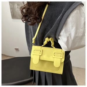 Detail of yellow minimalist crossbody bag with pleated handle and double buckles on model