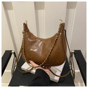 Detail of brown crescent shoulder bag with golden chain and zip closure on white books