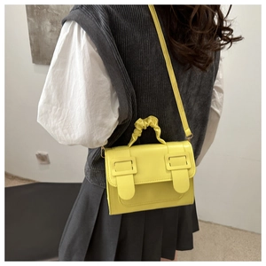 Detail of yellow crossbody bag featuring pleated cloud handle and decorative buckles