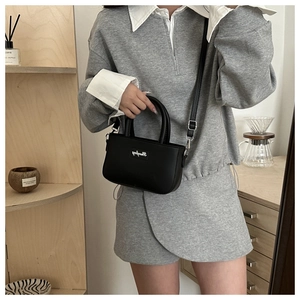 Detail of a matte black mini crossbody bag with top handles and adjustable strap