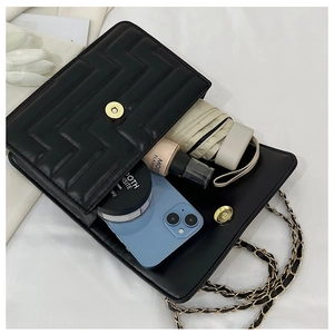Internal capacity of black quilted flap bag showing phone, makeup, and umbrella
