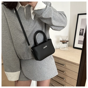 Dettaglio di una mini borsa tote in pelle nera minimalista con manico e tracolla lunga