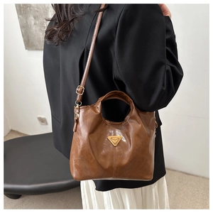 Detail view of the brown leather tote bag showing triangle metal logo and detachable strap