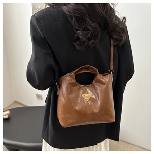 Detail of vintage brown leather bag with golden triangular logo and sleek shoulder strap