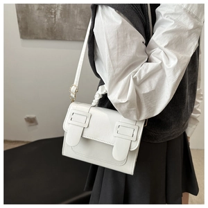Side view of white faux leather crossbody bag with pleated handle and metal buckles