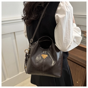 Detail of glossy oil wax leather tote bag featuring a metallic triangular logo plaque