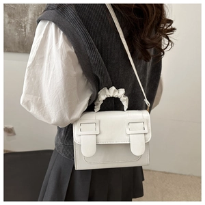White minimal leather crossbody bag with cloud pleat handle worn by a model in a stylish outfit