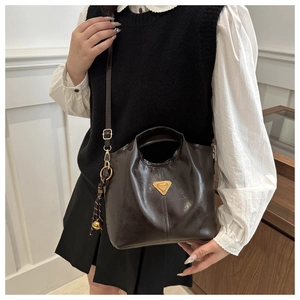 Detailed view of a dark brown oil wax leather bag with a golden triangle logo on model