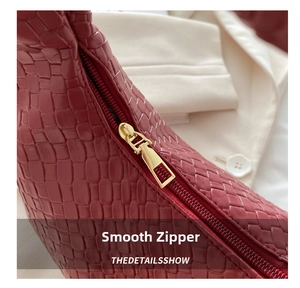Detail of burgundy leather bag showing woven texture and smooth golden metal zipper