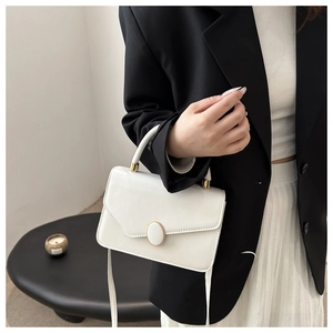 Detail einer minimalistischen cremeweißen Handtasche mit goldenem Oval-Drehverschluss