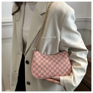 Detailed view of pink underarm bag with M-pattern print and gold chain strap on model