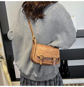 Detail of brown vintage crossbody bag with dual straps and metal fashion emblem