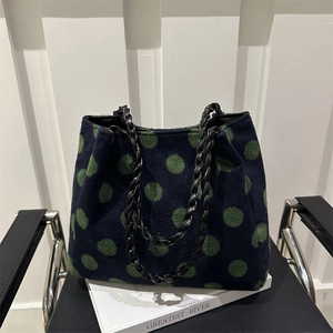 Blue felt tote bag with green polka dots and black woven chain strap on a white book