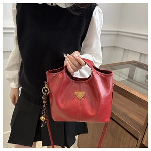 Detail view of red oil wax leather handbag featuring a gold triangle metal plaque and tassel