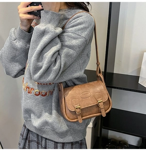Detail of retro brown leather shoulder bag with textured surface and gold buckle accents