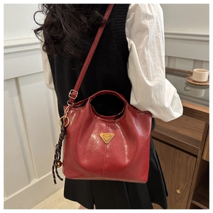 Detail of red wax leather handbag with golden metal logo and woven tassel pendant