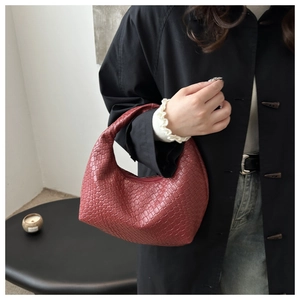 Detailed view of red woven leather hobo bag on model's arm in minimalist setting
