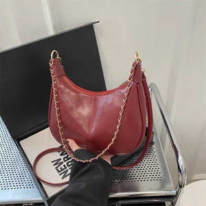 Deep red crescent tote bag with glossy finish and gold chain detail for women
