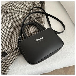 Detail of silver metallic logo and neat stitching on minimalist black leather handbag