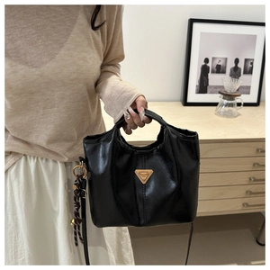 Detail of black wax leather tote featuring gold triangle logo and braided ball pendant