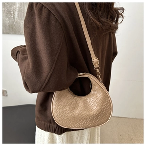 Detail of a beige crescent moon bag with crocodile pattern worn by a model in a coat