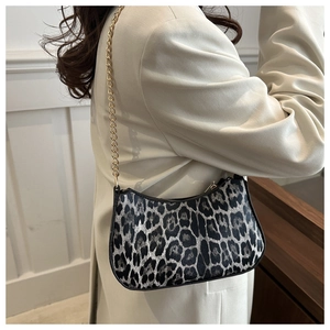 Detail of leopard print underarm bag with gold chain strap worn over a beige coat