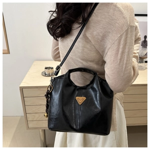 Detail of black wax leather tote bag with gold triangular logo and woven charm accessory