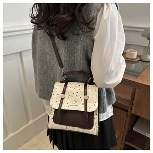 Polka dot backpack with vintage brown trim shown worn on a shoulder in a warm setting