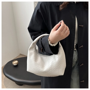 Detail of white woven hobo bag texture held by model wearing a black coat